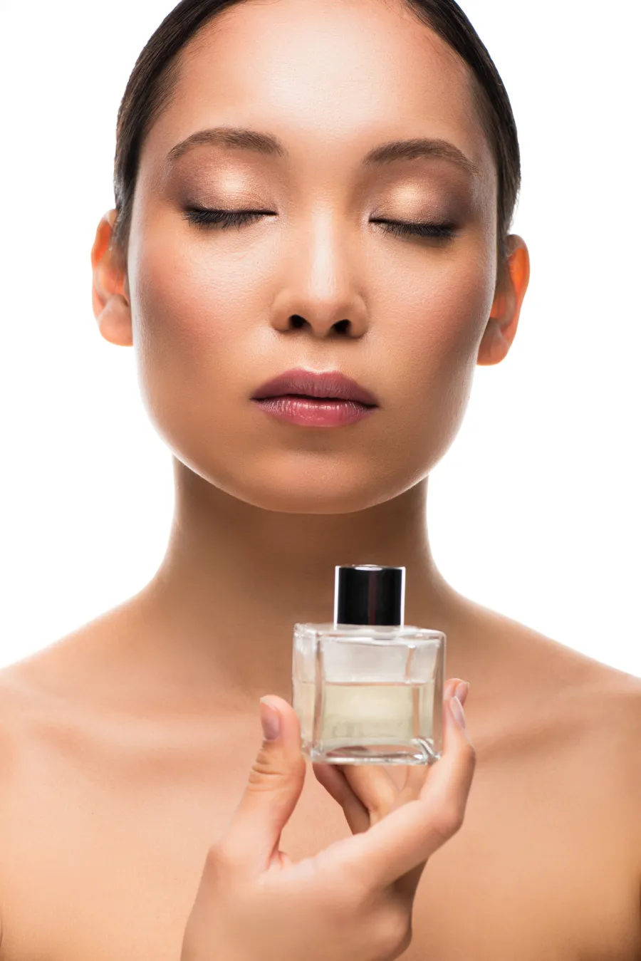 tender Asian woman with closed eyes holding perfume